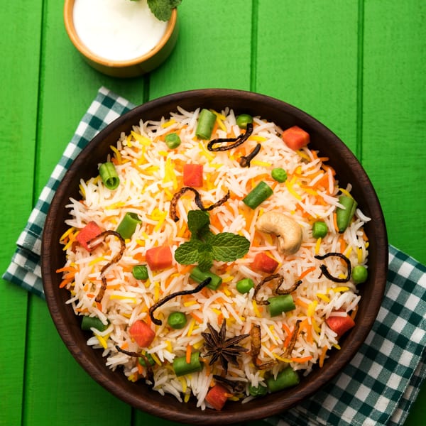 Vegetable Biryani with cashews, spices, and mint, served with raita on a green wooden table.