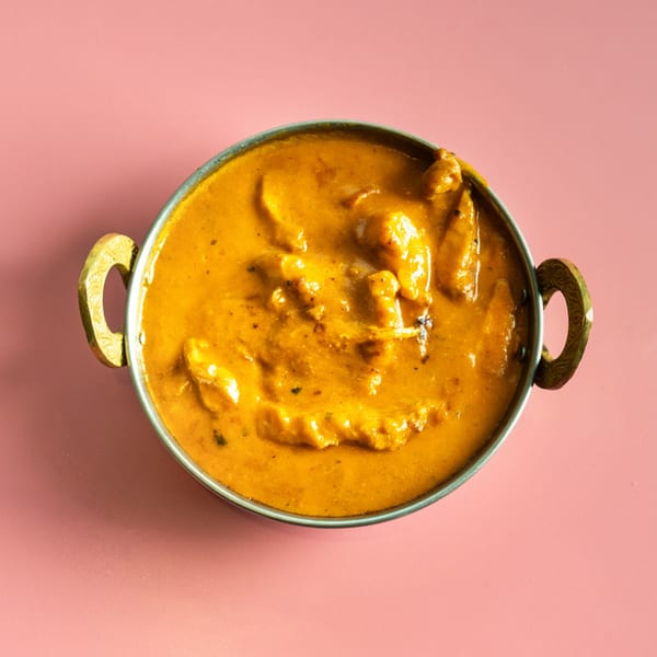 Overhead view of a metal bowl filled with orange chicken curry, on a pink background.