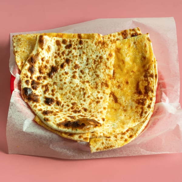 Golden-brown cheese quesadillas on a red plate with white parchment paper, against a pink background.