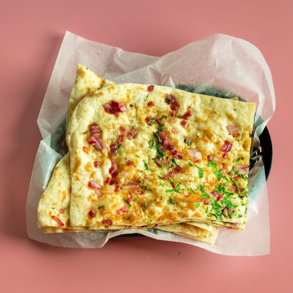Golden naan bread topped with chopped red onions and fresh green herbs in a basket.