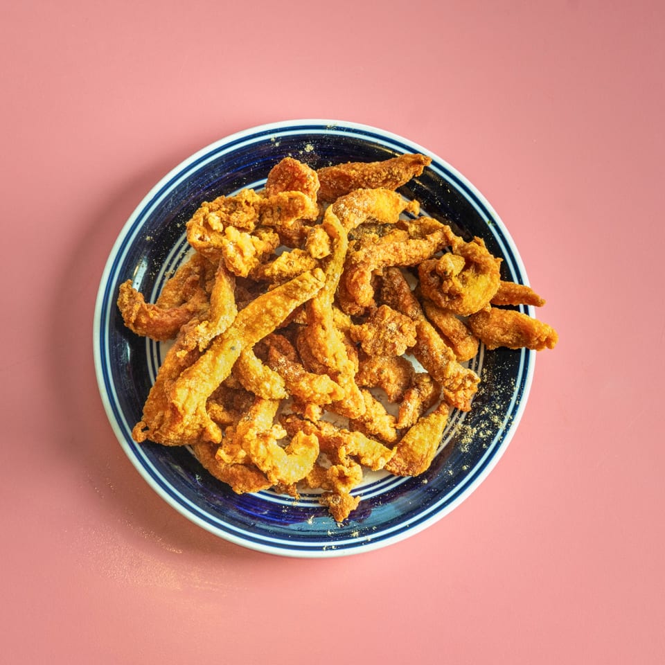 Crispy fried chicken skin or pork belly strips, seasoned with spices, on a blue and white plate.